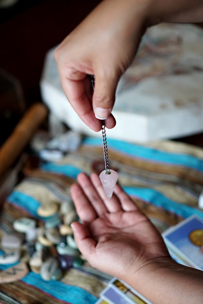 Crafting Captivating Headlines: Your awesome post title goes here Two hands using a rose quartz pendulum over tarot cards for divination purposes.